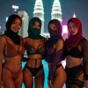Four women in hijabs posing by a rooftop pool with city skyline at night